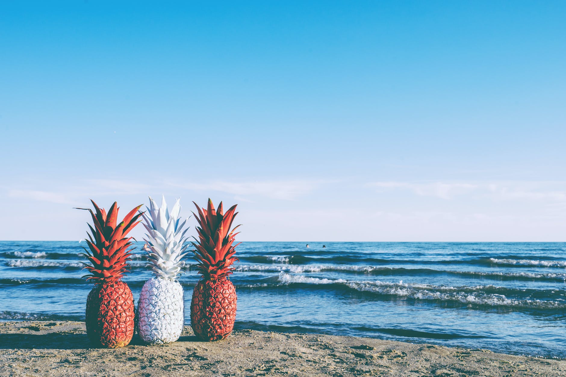 white and two red painted pineapples near on seashore