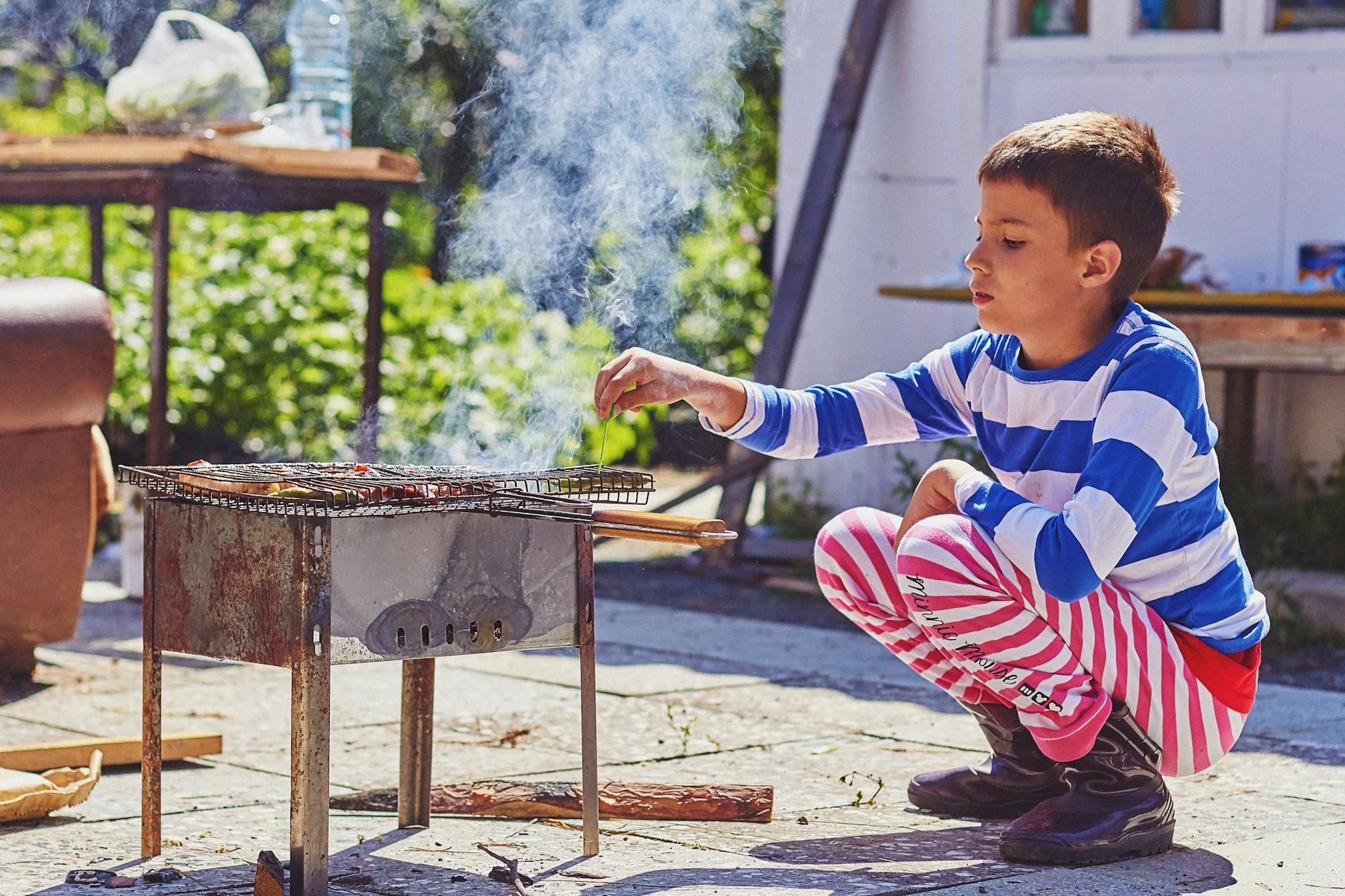 a boy sitting beside the barbecue grill